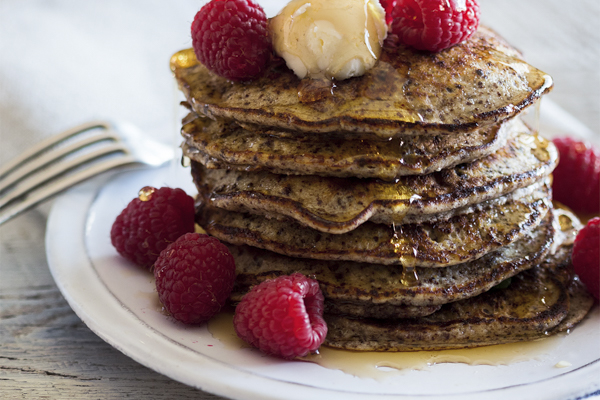 a tall stack of chocolate ricotta pancakes with raspberries and syrup