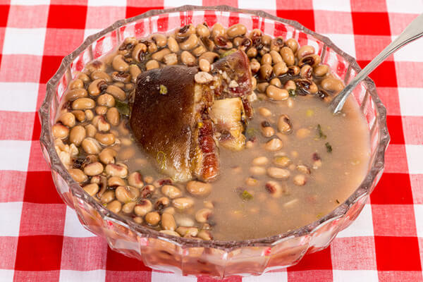 bowl of black eyed peas with ham hock on a checkered tablecloth